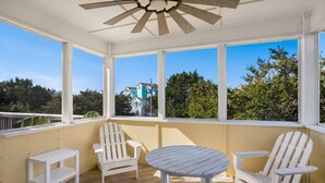 A covered outdoor area with a wooden floor, white chairs, a small table, and large windows offering views of houses and trees. - 4 br, loft, dog friendly, pool firepit! (Avon)
