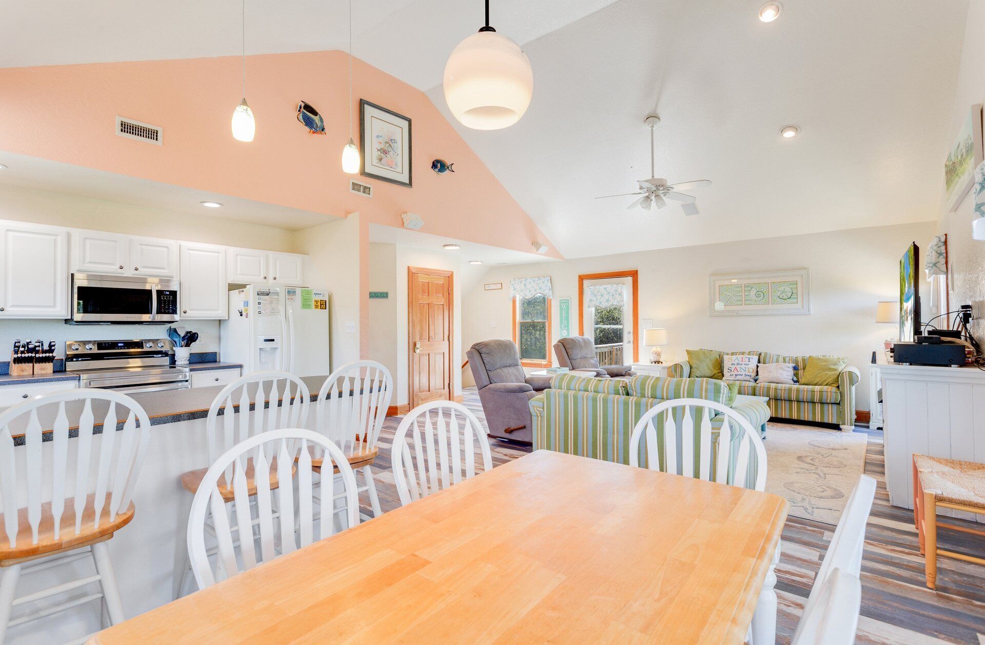 A modern kitchen with white cabinets, a microwave, and a stove. There is a dining area with a wooden table and white chairs.