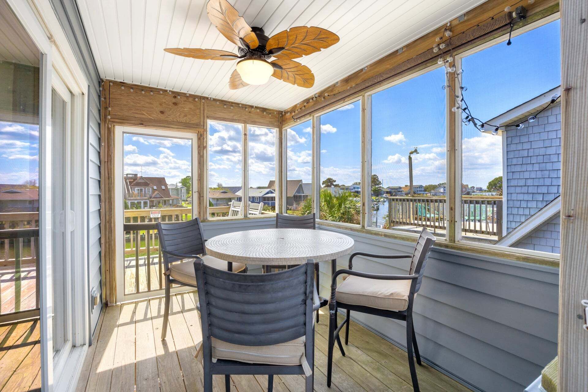 A covered patio with a round table and chairs, large windows, and a ceiling fan.