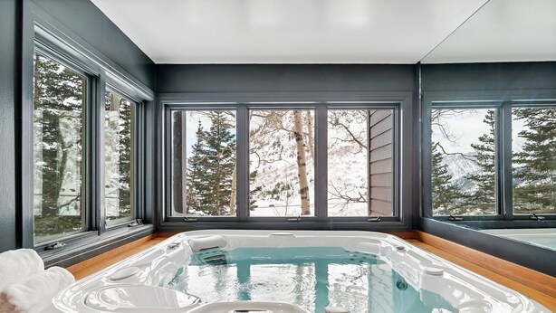 A modern spa room with a hot tub, large windows, and a view of trees and mountains. - Ski in/Ski Out to Snowbird in Gorgeous Unit with Hot Tub and Beautiful Views (Alta)