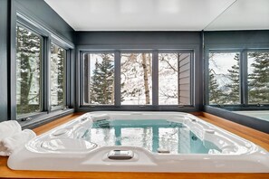 A modern spa room with a hot tub, large windows, and a view of trees and mountains.