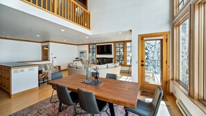A spacious living area with a wooden dining table, black chairs, a sofa, and a TV. - Ski in/Ski Out to Snowbird in Gorgeous Unit with Hot Tub and Beautiful Views (Alta)