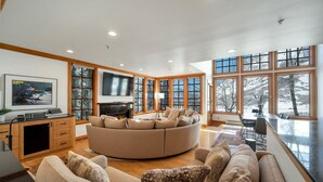 A spacious living room with a large round sofa, a fireplace, and a television. - Ski in/Ski Out to Snowbird in Gorgeous Unit with Hot Tub and Beautiful Views (Alta)