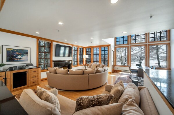 A spacious living room with a large round sofa, a fireplace, and a television.