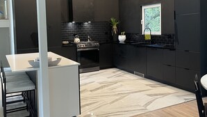 A modern kitchen with dark cabinetry, a white countertop, and a built-in stove. - Minimalist sauna retreat  (Brighton)