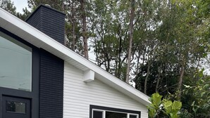 A modern two-story house with a black and white exterior, a front door, and a small front yard with two large planters. - Minimalist sauna retreat  (Brighton)