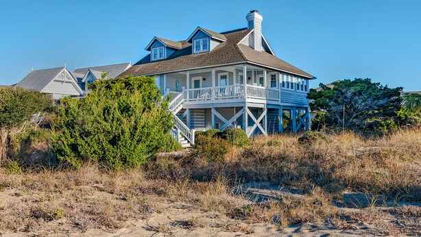 Ein großes, zweistöckiges Haus mit Balkon, umgeben von trockenem Gras und Bäumen.