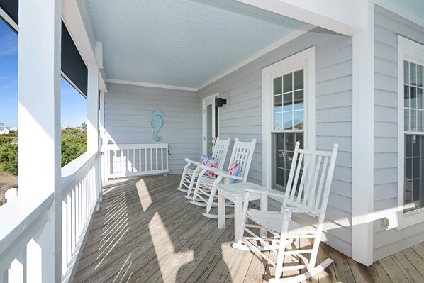A porch with white wooden railings and rocking chairs, a seahorse decoration, and a clear view of the surrounding landscape. - Upscale renovated beach cottage across from South beach! (Bald Head Island)