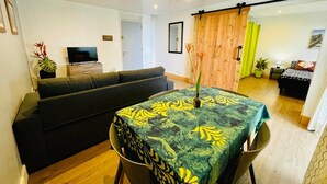 Un salon avec un canapé, une table à manger recouverte d’une nappe à motifs, un téléviseur et une porte coulissante donnant sur une autre pièce.