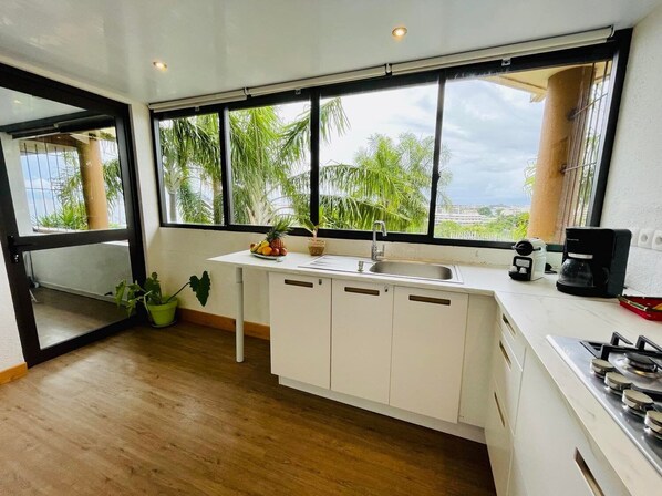 A modern kitchen with a large window, white cabinets, a sink, and a stove.