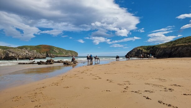 A beach with horses and riders, rocky cliffs, and a clear sky. - Apartamento La Muga Azul (Celorio (Llanes))