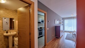 A modern apartment with a wooden door leading to a bathroom, a kitchenette, and a living area with a sofa and a dining table. - Apartamento La Muga Azul (Celorio (Llanes))