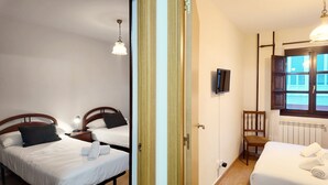 A hotel room with two beds, a TV, a chair, and a window with a view. - Apartamento Vacacional La Rula (Llanes)