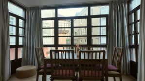 A room with a large window, a table with chairs, and a small ottoman. - Apartamento Vacacional La Rula (Llanes)