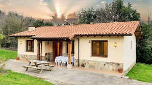 Una casa de una planta con techo de tejas, cimientos de piedra y un patio con mesa y sillas.