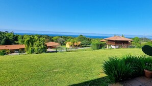 A well-maintained lawn with a cactus in the foreground, a wooden deck, and a view of the sea in the background. - [1] (Ovio)