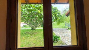 A window with a view of a tree, a stone patio, and a grassy area. - [1] (Ovio)