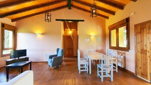 A cozy room with a wooden ceiling, a dining table with chairs, a sofa, and a television. - [1] (Ovio)