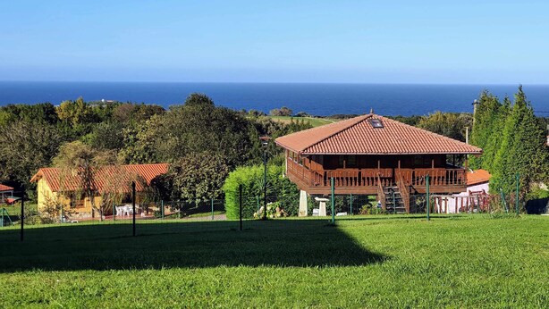 A building with a red-tiled roof, a wooden deck, and a view of the sea. - [1] (Ovio)