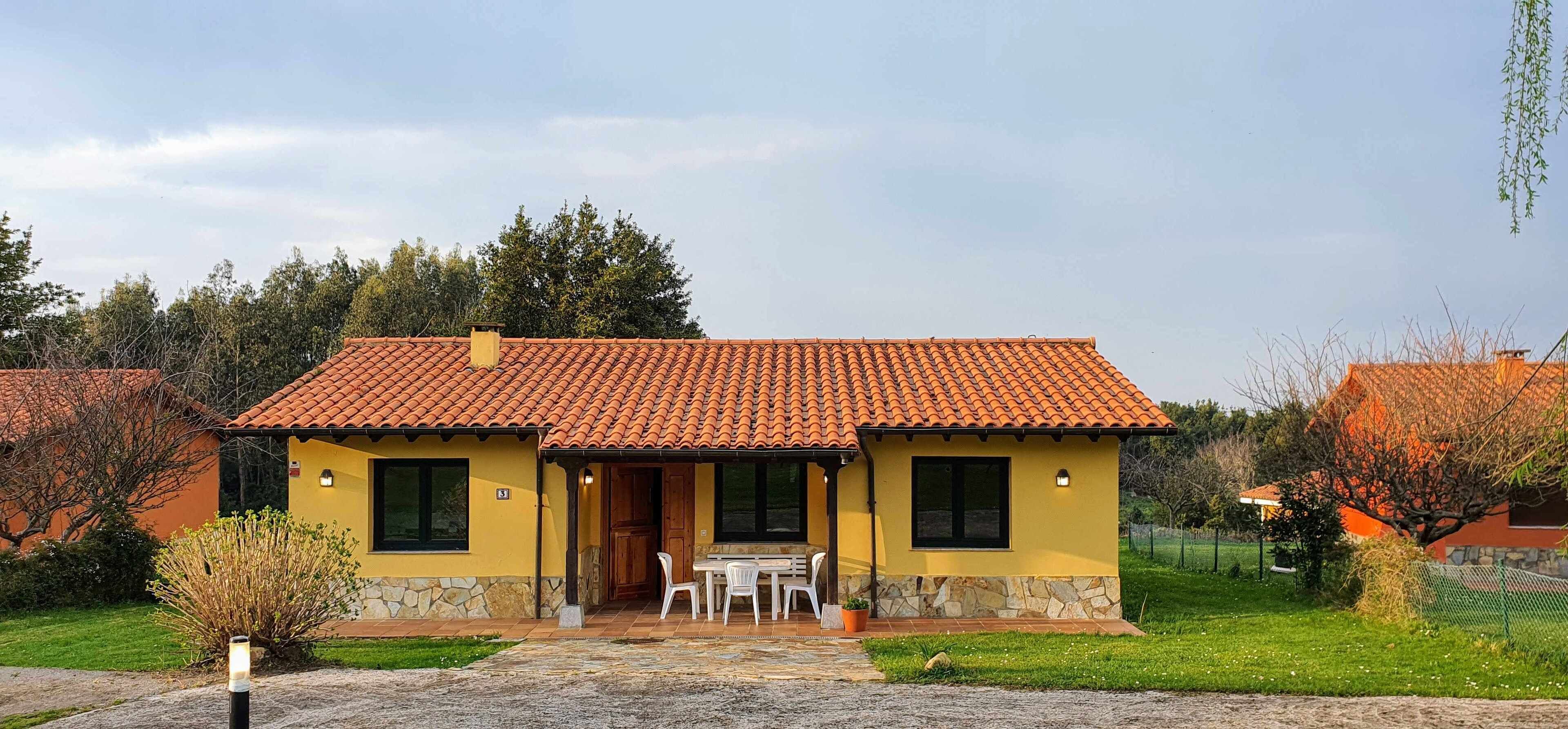 A two-story house with a tiled roof, a stone foundation, and a small patio with a table and chairs.