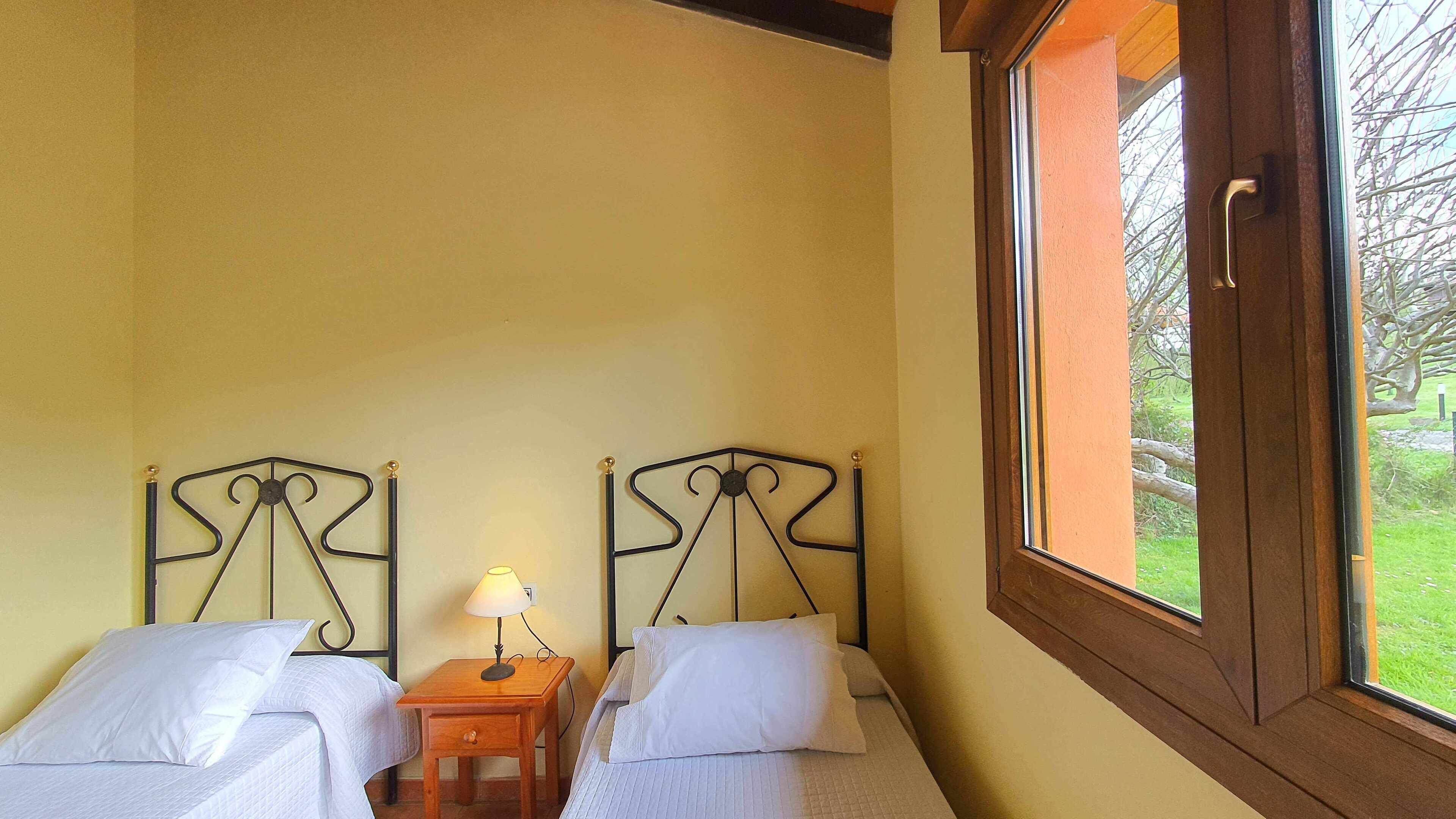 A room with two single beds, each with a headboard and a bedside table with a lamp.
