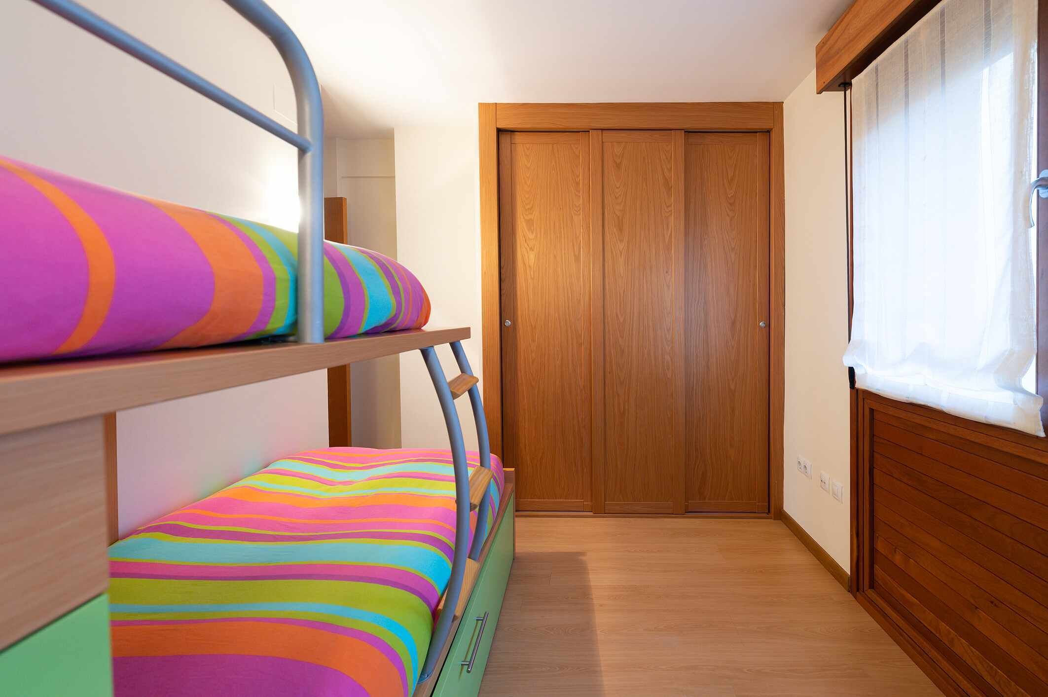 Une chambre avec un lit superposé, une armoire en bois et une fenêtre avec des rideaux.