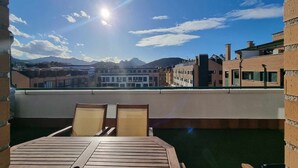 A rooftop terrace with a wooden table and chairs, offering a view of buildings and mountains in the distance. - La Terraza del Paraiso (Posada De Llanes)