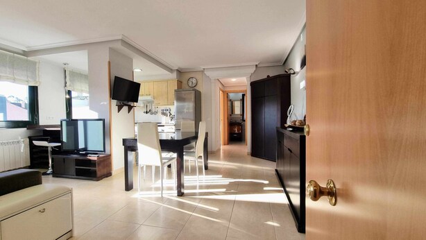 A modern kitchen with a dining area, a TV, and a clock on the wall. - La Terraza del Paraiso (Posada De Llanes)