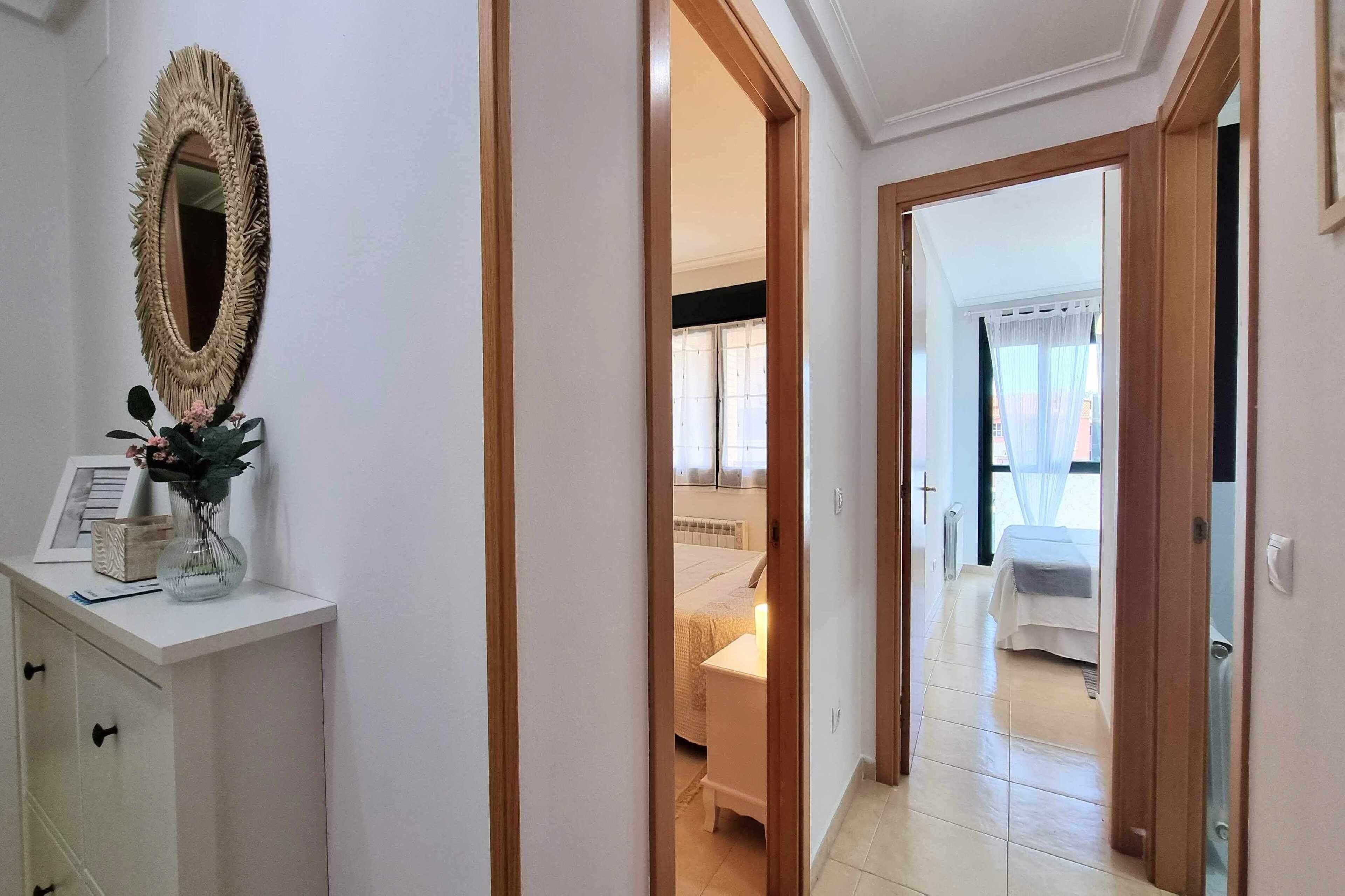 Un couloir menant à une chambre à coucher équipée d’un lit, d’une table de chevet et d’un miroir.
