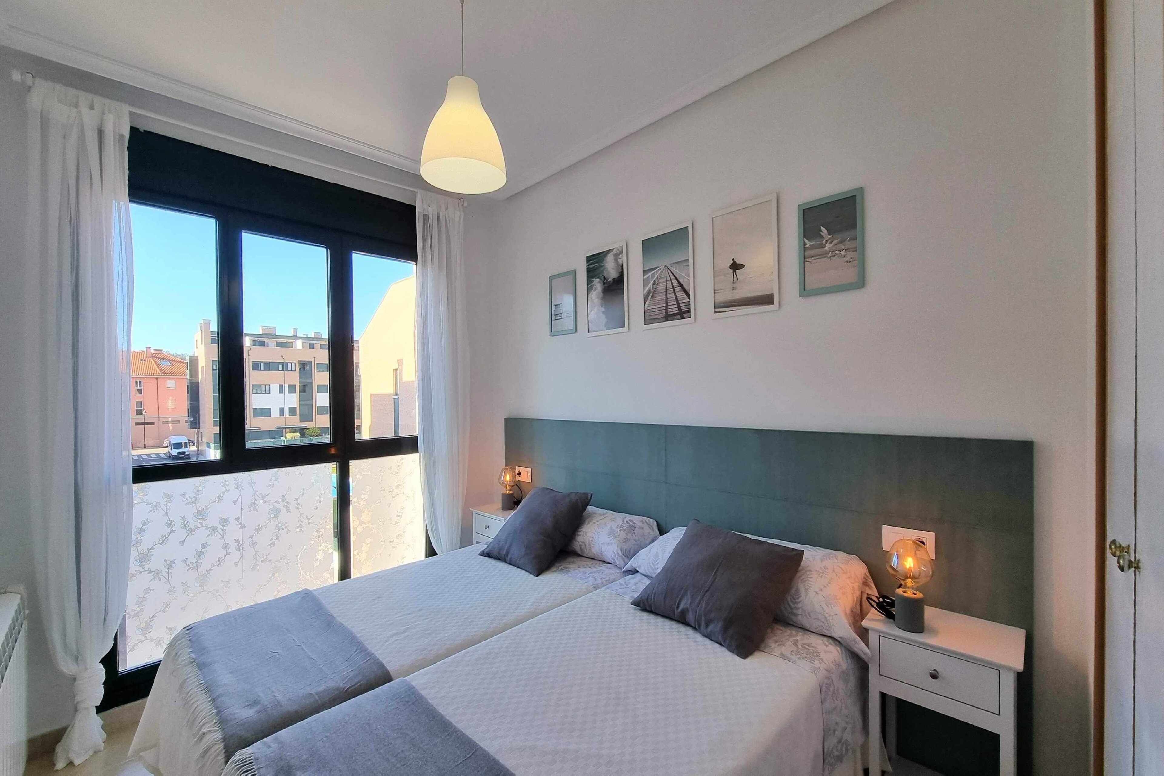 Une chambre d’hôtel avec deux lits, une grande fenêtre avec des rideaux, une table de chevet avec une lampe et des œuvres d’art murales.