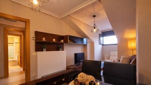 Un salon moderne avec une table basse en bois foncé, un téléviseur et un canapé. On y trouve des étagères ornées d’objets décoratifs et une lampe.