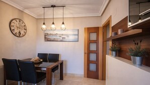 Un coin repas avec une table et des chaises en bois, une horloge, des lampes suspendues et un tableau au mur.