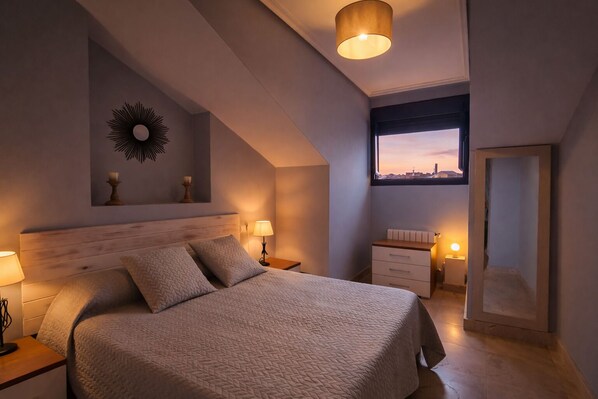 A modern bedroom with a large bed, bedside lamps, a nightstand, a dresser, a mirror, and a view of the city at sunset.