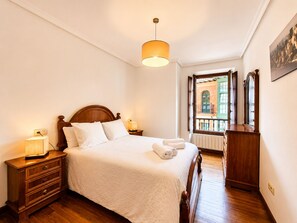 Une chambre à coucher avec un lit en bois, des lampes de chevet, une commode et une vue sur un balcon.
