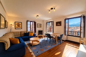 A living room with a sofa, a dining table, chairs, a TV, and large windows with a view.