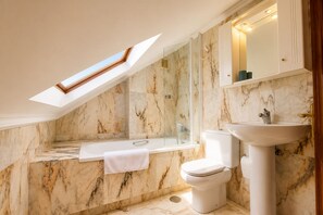 A bathroom with a skylight, a bathtub, a toilet, and a sink.