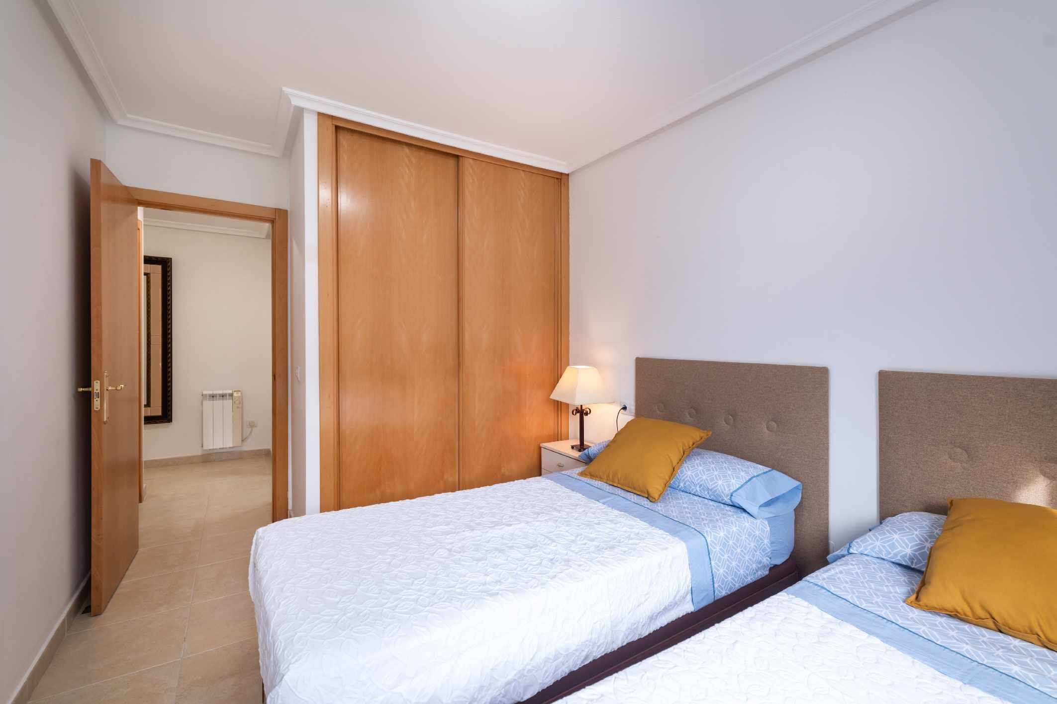 Ein Hotelzimmer mit zwei Betten, einem Holzschrank, Nachttischen mit Lampen und Blick auf den Flur.