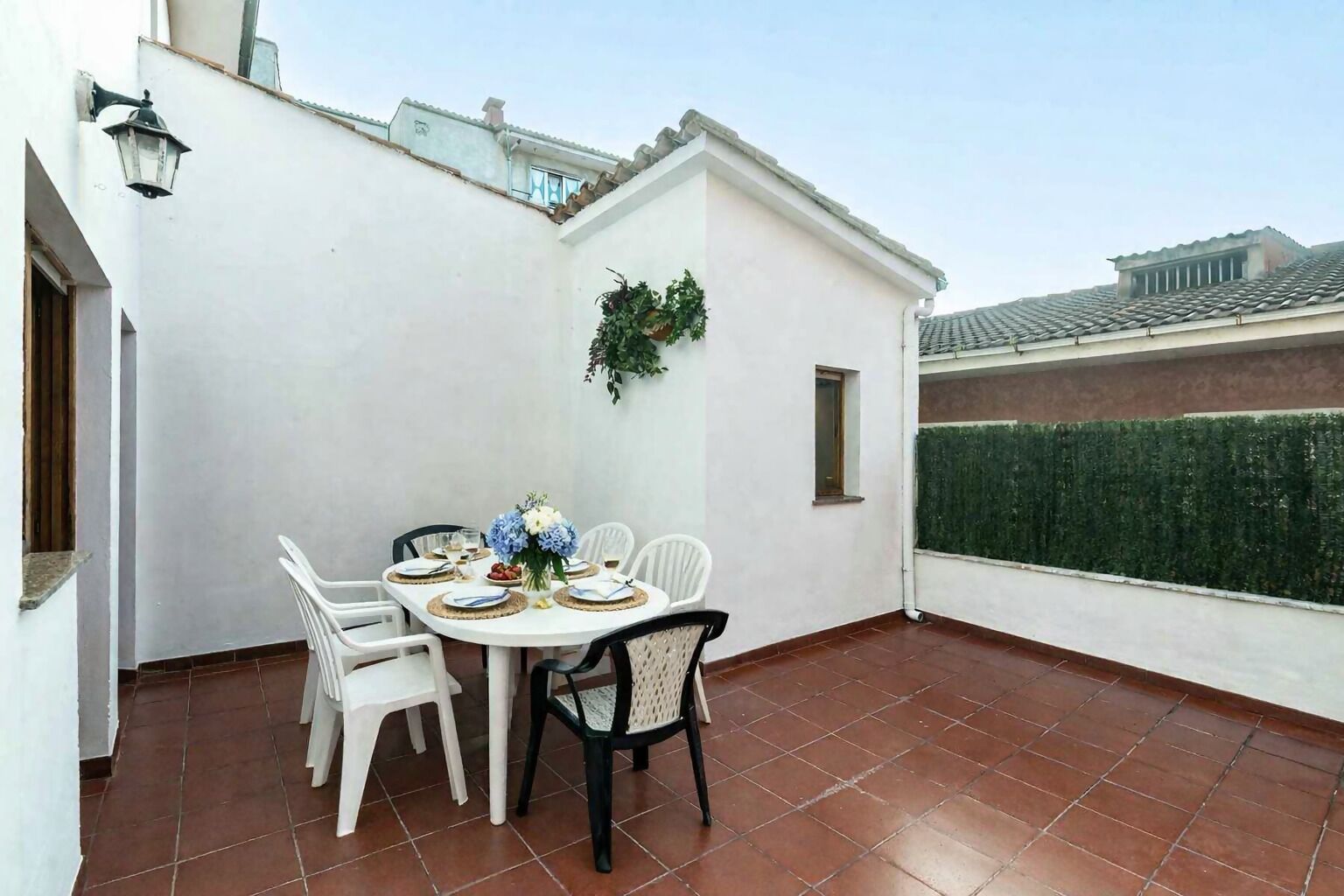 A small patio with a round table set for four, surrounded by white chairs.