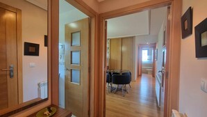 Un couloir mène à une salle à manger équipée d’une table et de chaises, de portes en bois et d’un radiateur fixé au mur.