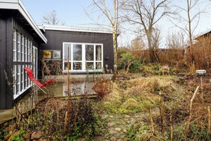 Een modern huis met een groot raam, een houten terras en een rode stoel.