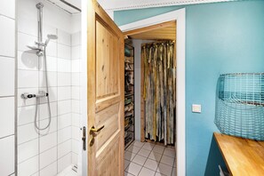 Un baño con ducha, una puerta de madera, piso de baldosas y pared azul.