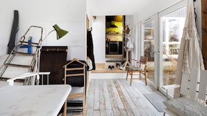 Une pièce avec un plancher en bois, une table blanche, une chaise, un porte-manteau suspendu et une porte donnant sur un espace cuisine.