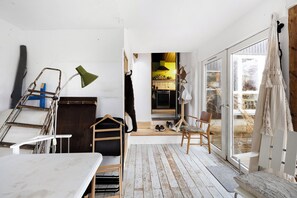 Una habitación con piso de madera, una mesa blanca, una silla, un perchero y una puerta que da a una zona de cocina.