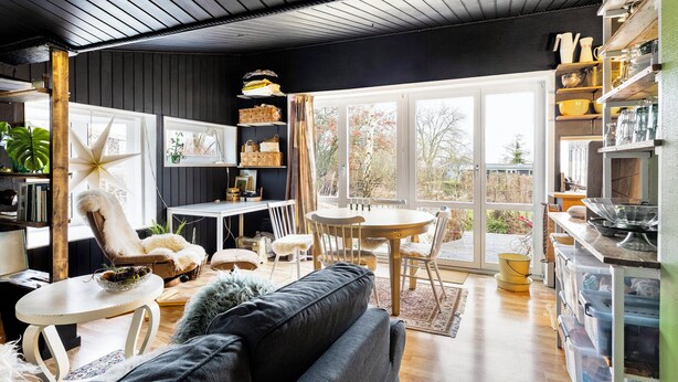 Un salon confortable avec un canapé, une table à manger et des chaises. On y trouve une bibliothèque, une fenêtre avec des rideaux et une vue sur l’extérieur.
