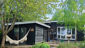 Une maison avec un hamac, une terrasse et un jardin.