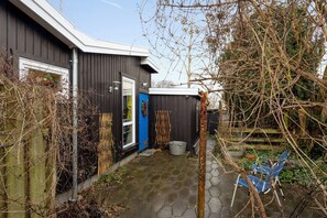 Una casa de exterior oscuro, con una puerta azul, un pequeño jardín con una silla metálica y una valla de madera.