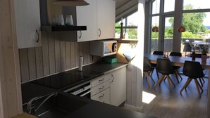 A modern kitchen with a black countertop, white cabinets, and a dining area with a table and chairs. - Cottage in Grønninghoved with view (Sjølund)