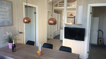 A modern kitchen with a built-in oven, a large flat-screen TV, and a dining area with a wooden table and chairs.