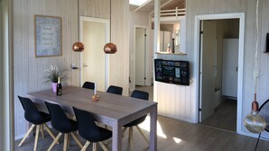 A dining area with a wooden table and chairs, a potted plant, and a mounted television displaying a program. - Cottage in Grønninghoved with view (Sjølund)