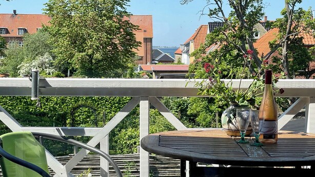 En balkong med ett bord, en stol, en flaska vin och en vas med blommor.